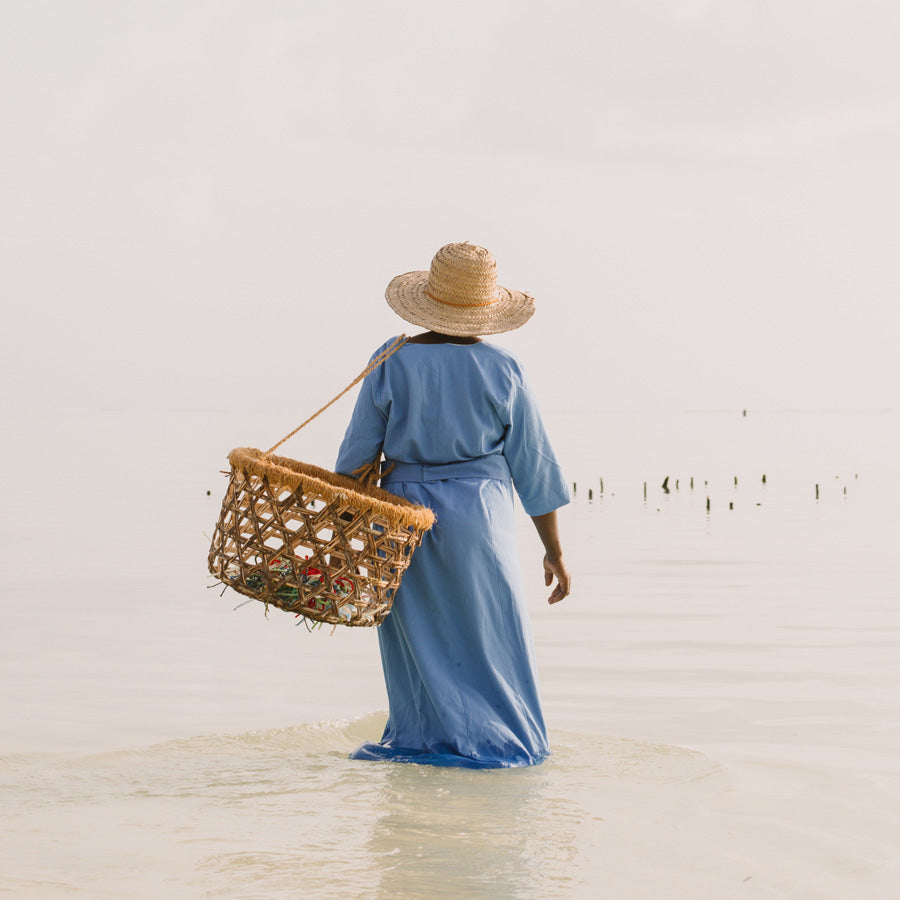 A Mwani Zanzibar Mama carrying a harvesting basket and looking towards the ocean.
